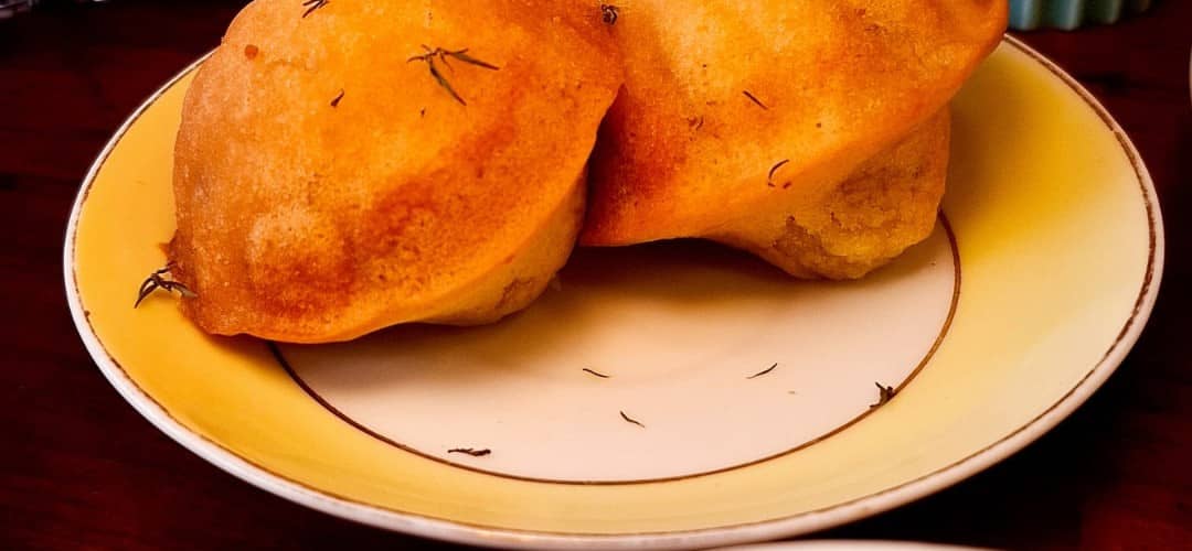 Duas madeleines salpicadas de tomilho num prato amarelo de borda dourada.