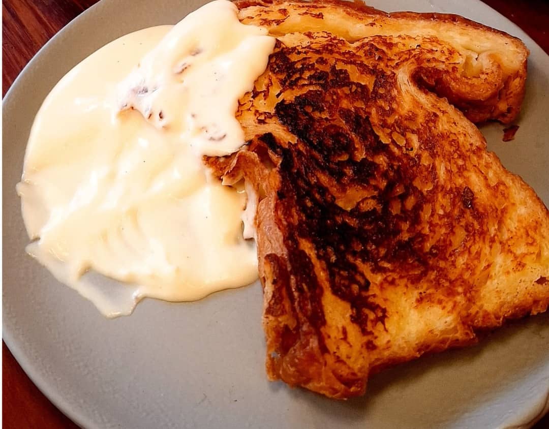 Fatia de pain perdu tostada, com creme anglaise escorrendo no prato.
