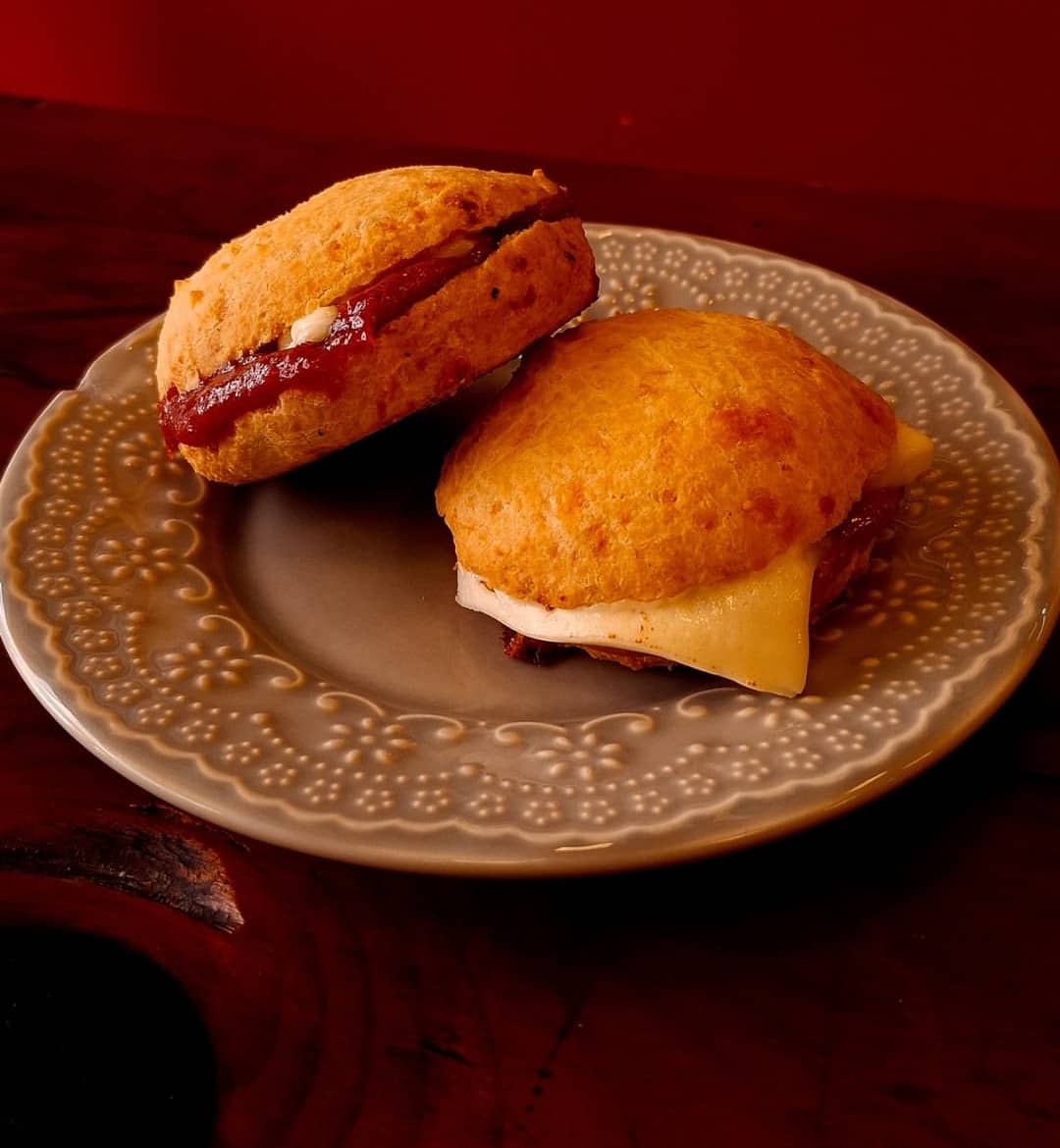 Dois pães de queijo recheados num prato de cerâmica cinza, diante da parede vermelha.
