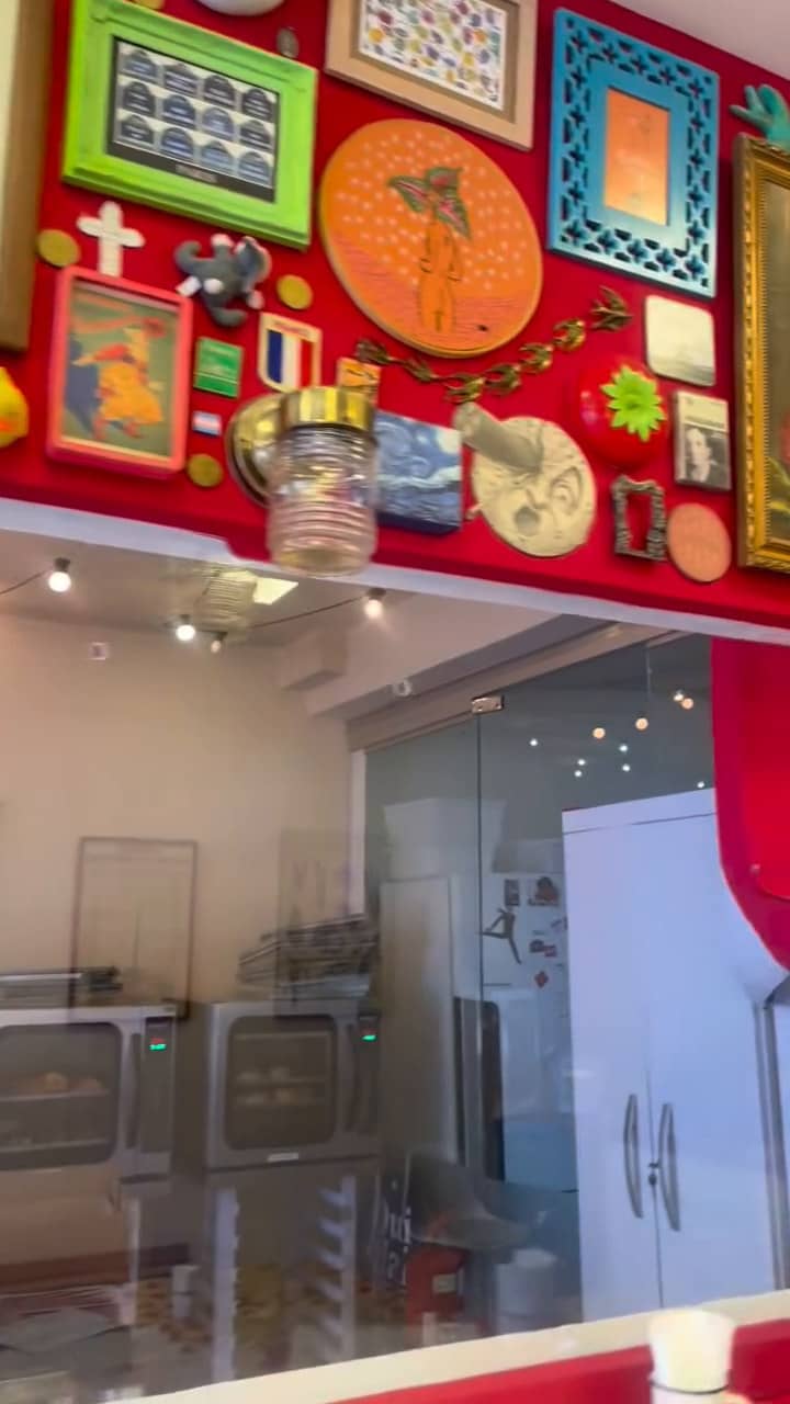 Molduras coloridas na parede vermelha, acima do vidro que mostra a cozinha.